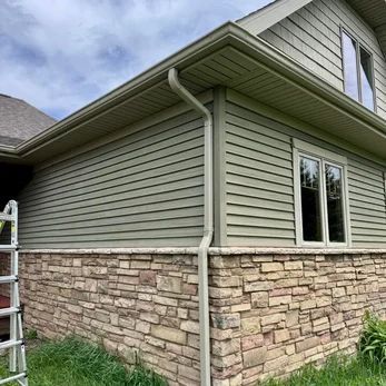 Exterior of a house with green siding, stone veneer, and a white downspout under the eaves