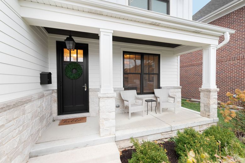 A white house with a black door and a porch with chairs and a table.