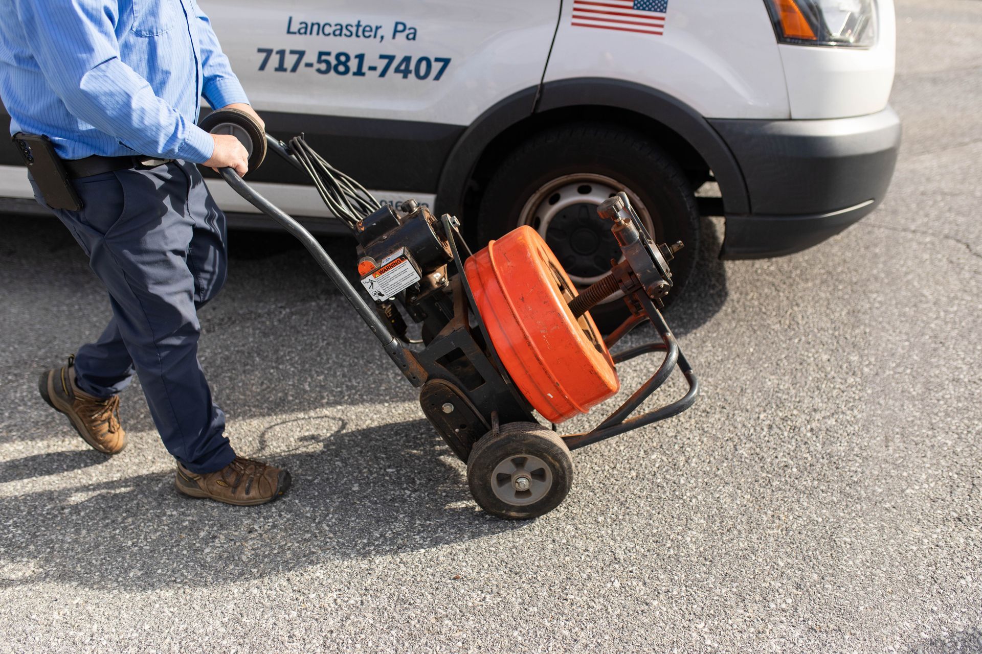 Plumber pulling a drain cleaning machine from a white van in a parking lot.
