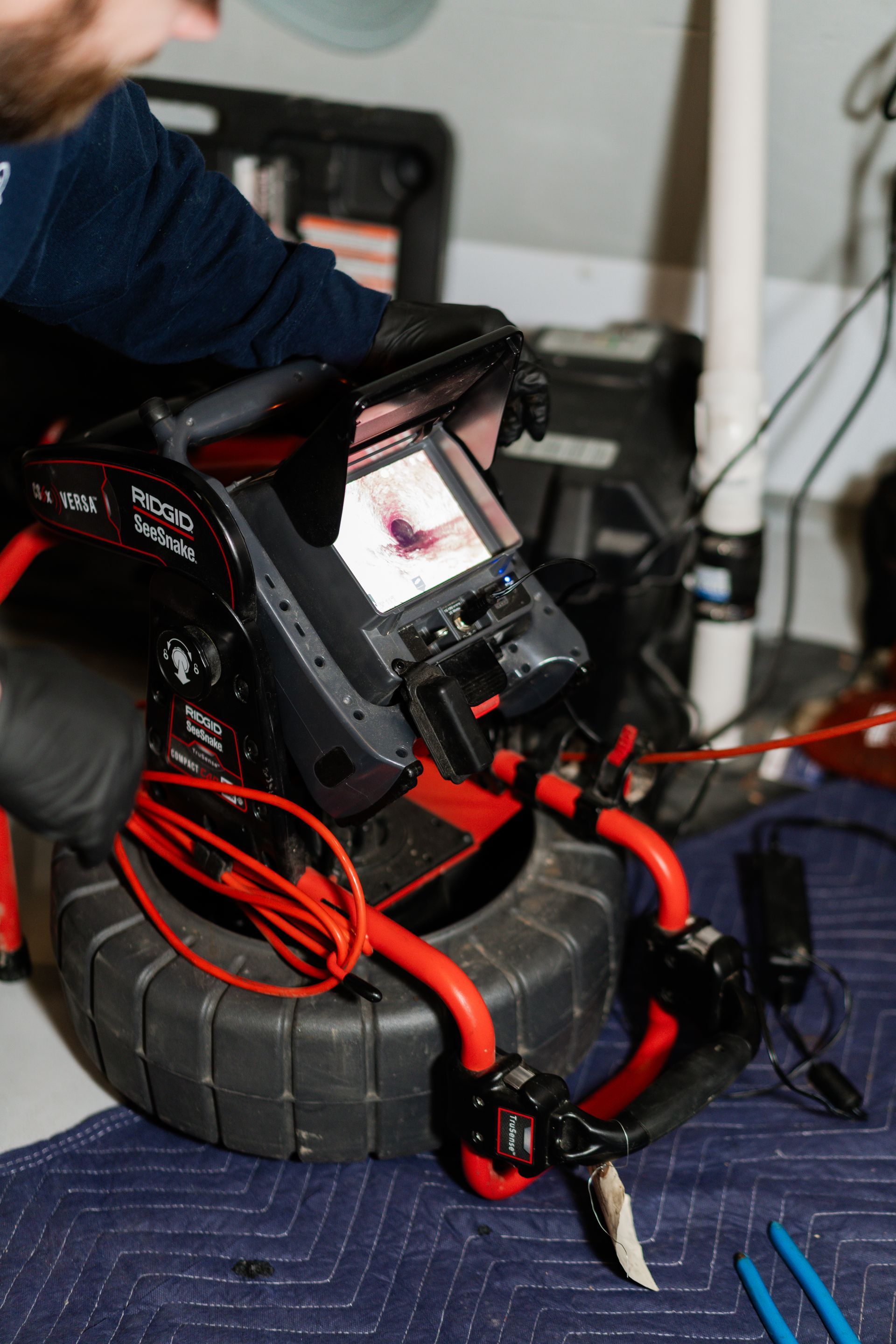 A technician uses a portable, red-and-black video pipe inspection camera to view an internal pipeline blockage on a screen.