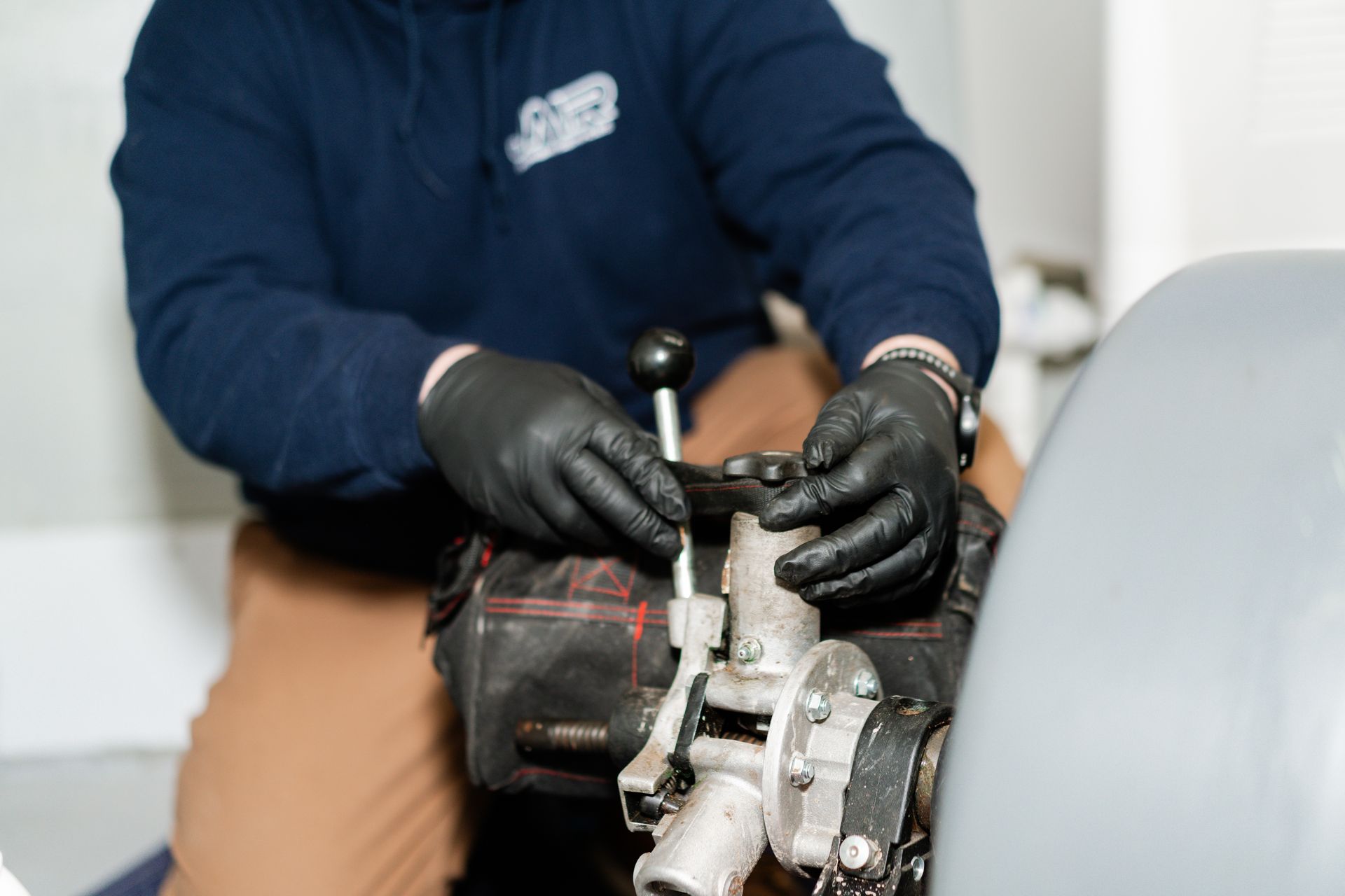 A worker wearing black gloves uses a tool to tighten or adjust the component of a mechanical device.