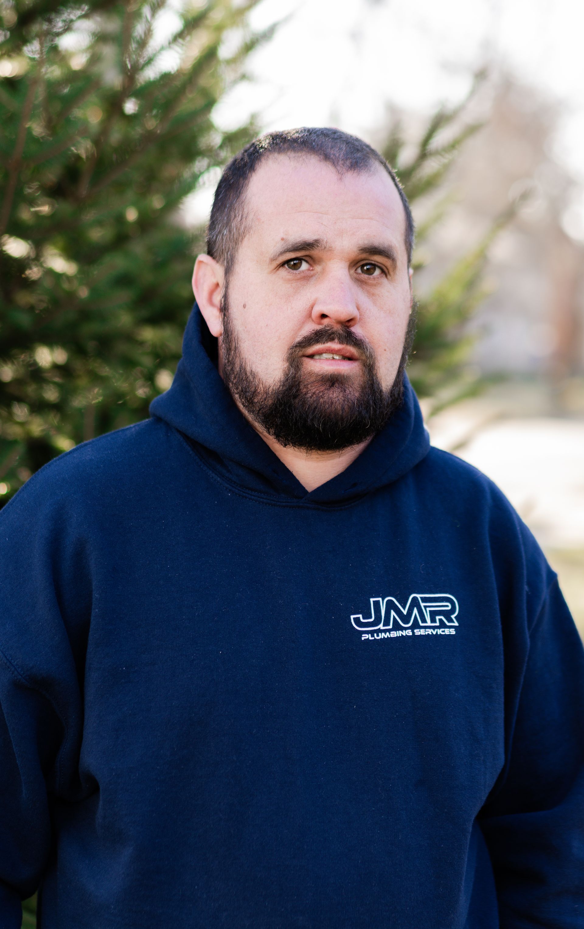 A person with a beard wearing a dark blue hooded sweatshirt with a white 