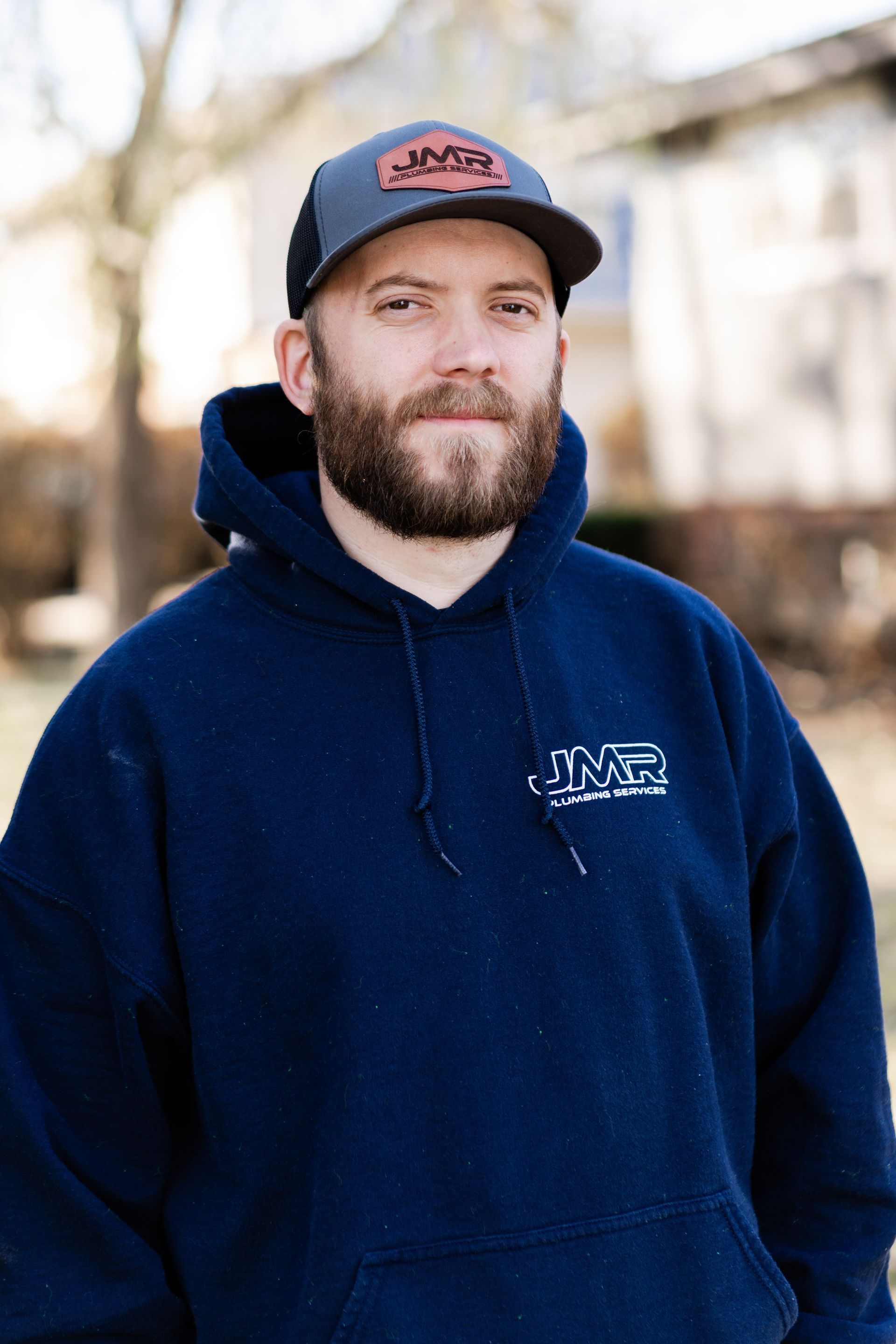 A person wearing a blue hooded sweatshirt with a logo and a dark baseball cap stands outdoors, facing the camera.