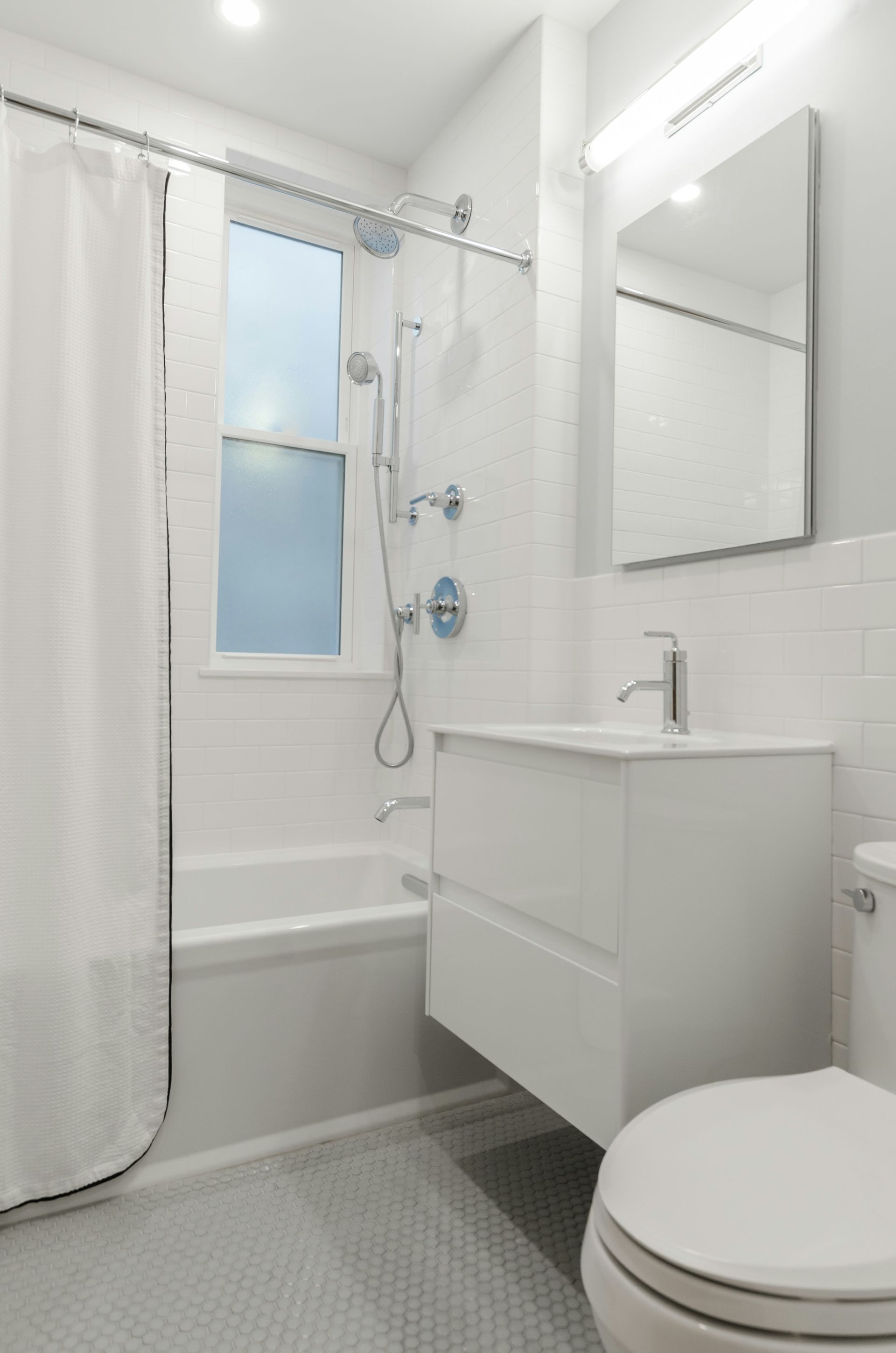 A bright, modern white bathroom featuring a floating vanity, a bathtub with a showerhead, and a rectangular mirror.