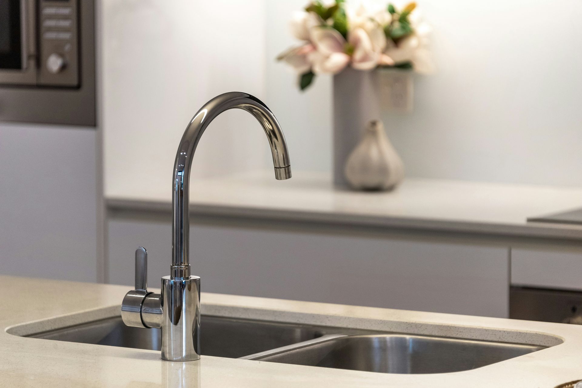 A modern kitchen island with a chrome arched faucet, double stainless steel sink, and a vase of flowers in the background.
