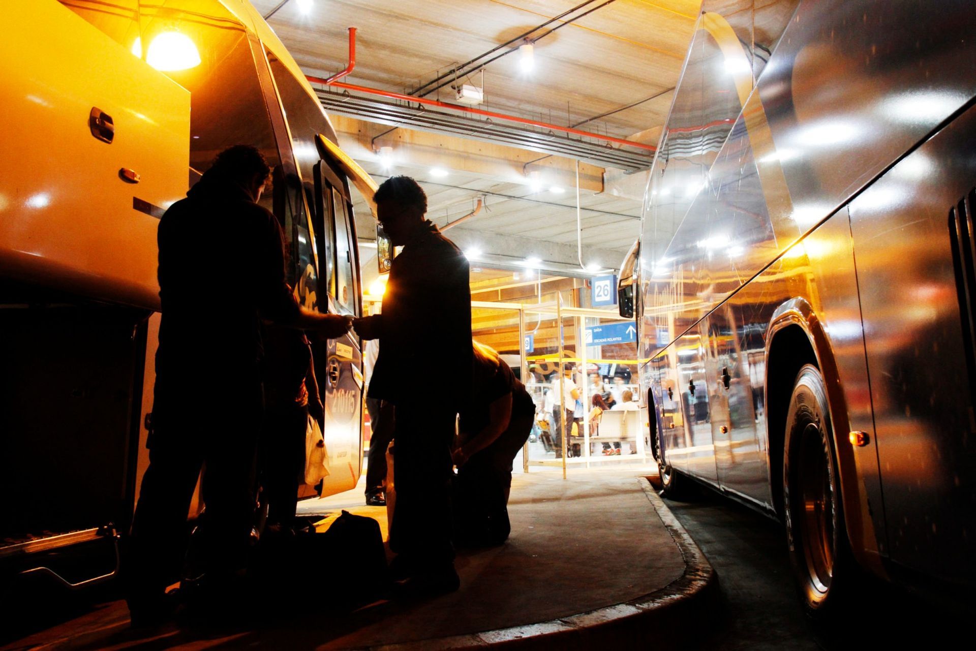 Silhuetas ao lado de ônibus em uma garagem de ônibus pouco iluminada.