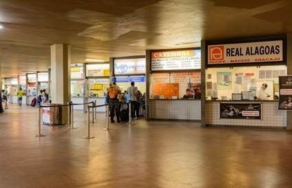 Bilheterias do terminal rodoviário, várias com pessoas esperando, sob um teto de concreto.