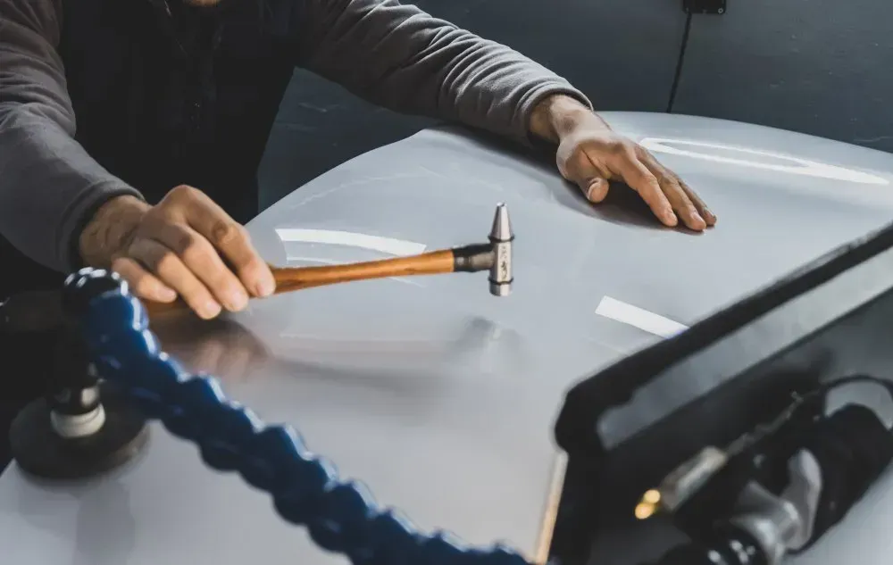 Person Using a Hammer to Repair a Dent on a Car Hood, Working With Repair Tools — Coastal Collision Repairs in Buderim, QLD