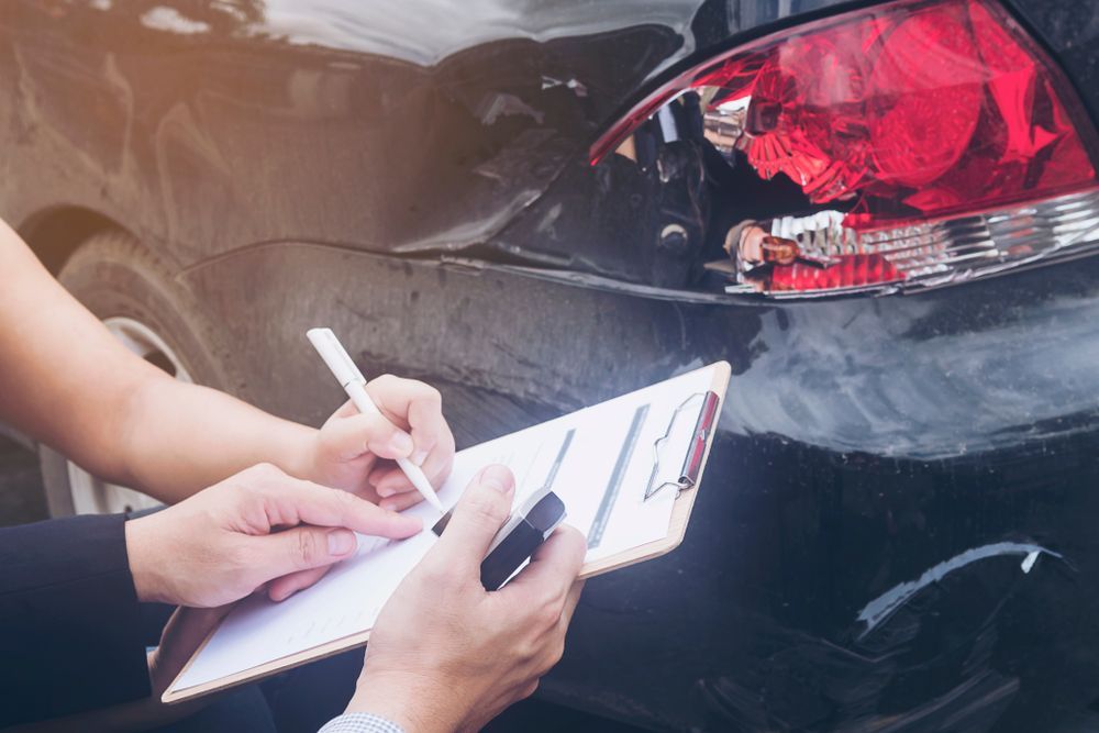 Person Writing on Clipboard Next to Damaged Car, Examining Rear Taillight — Coastal Collision Repairs in Buderim, QLD