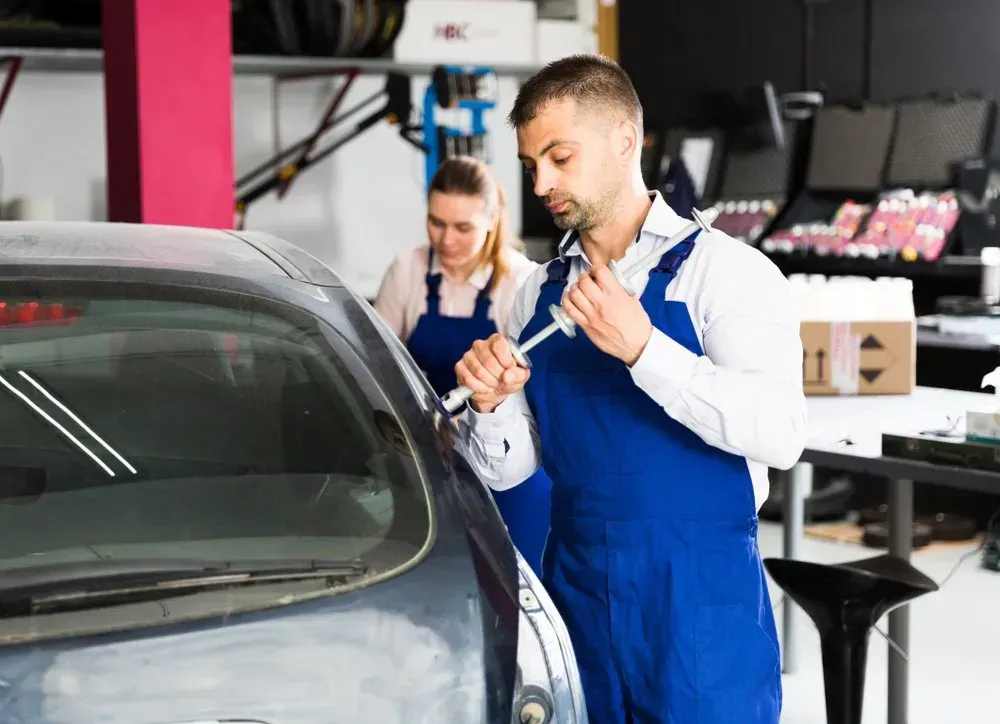 Mechanic in Blue Overalls Working on a Car in a Garage, a Coworker in Background — Coastal Collision Repairs in Buderim, QLD