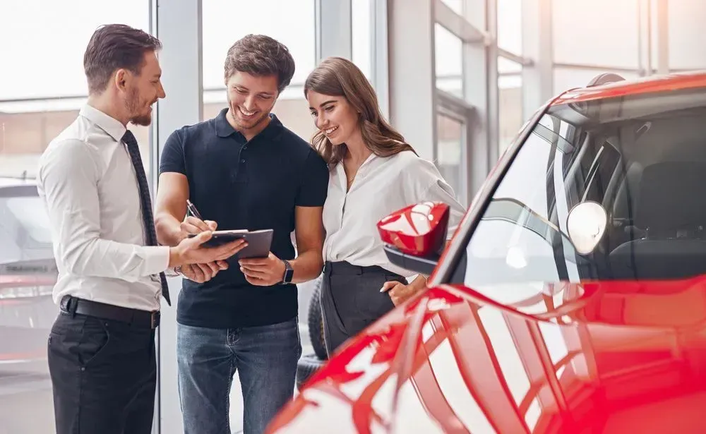Car Salesperson Showing Paperwork to a Couple Next to a Red Car in a Showroom — Coastal Collision Repairs in Buderim, QLD
