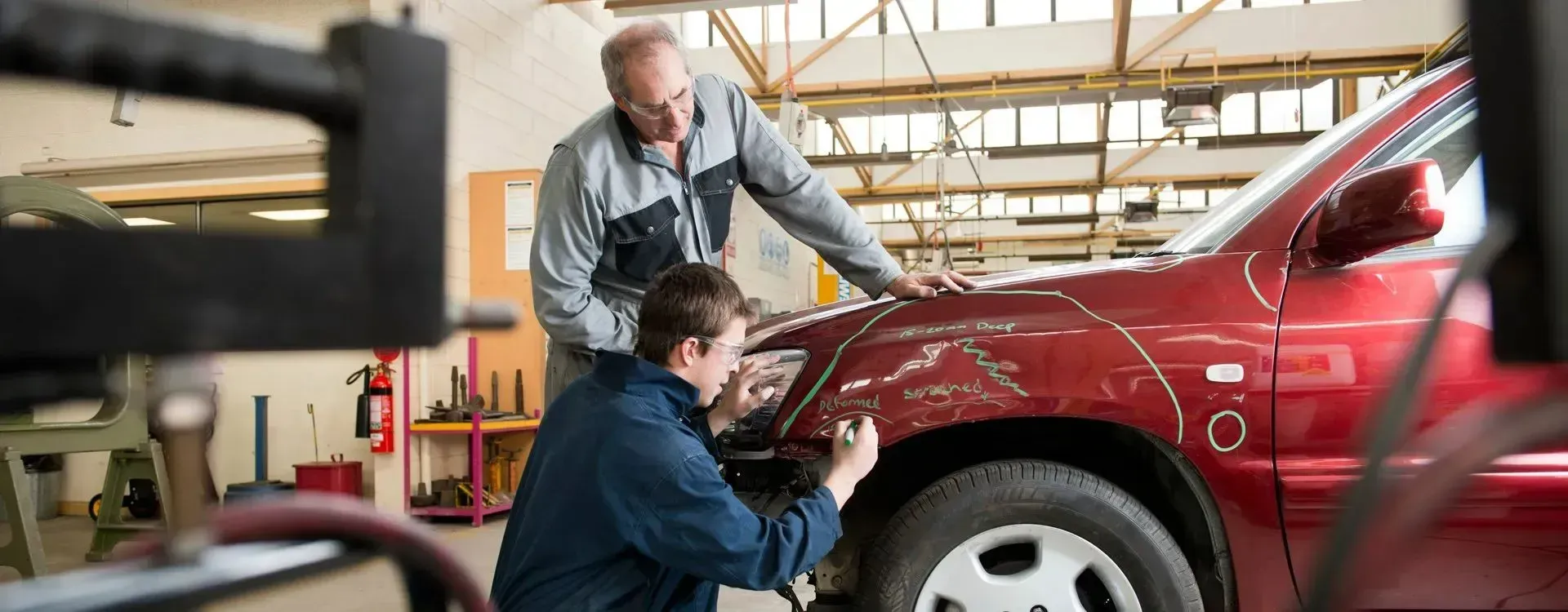 Two Auto Mechanics Inspect a Red Car's Damaged Fender in a Workshop — Coastal Collision Repairs in Buderim, QLD