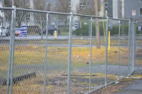 Chain-link fence around a small grassy lot with a yellow post and buildings in the background. Chain-link fence around a small grassy lot with a yellow post and buildings in the background.