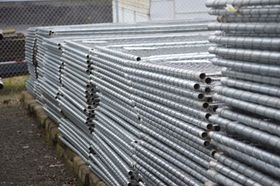 Stacked silver metal pipes or conduit bundled outdoors beside a fence Stacked silver metal pipes or conduit bundled outdoors beside a fence
