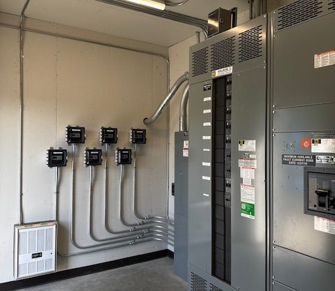 Electrical panel room with gray panels, conduit, and meters.