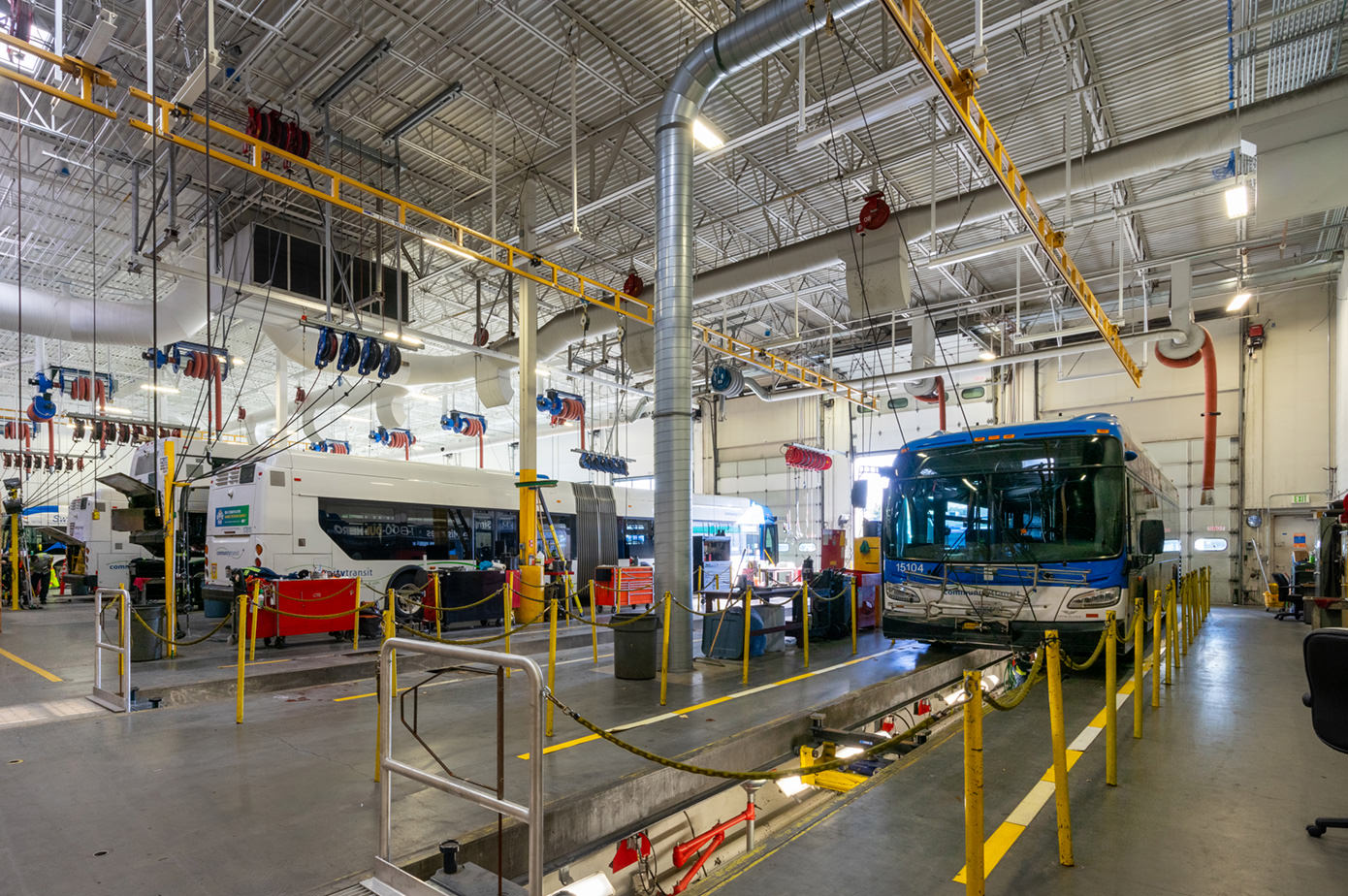 Bus maintenance garage with two buses, overhead utilities, and service equipment.