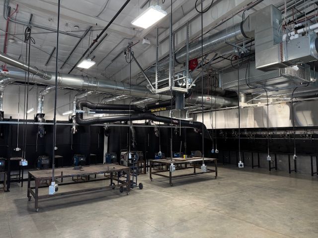 A welding workshop interior with multiple work stations, ventilation, and overhead lighting.