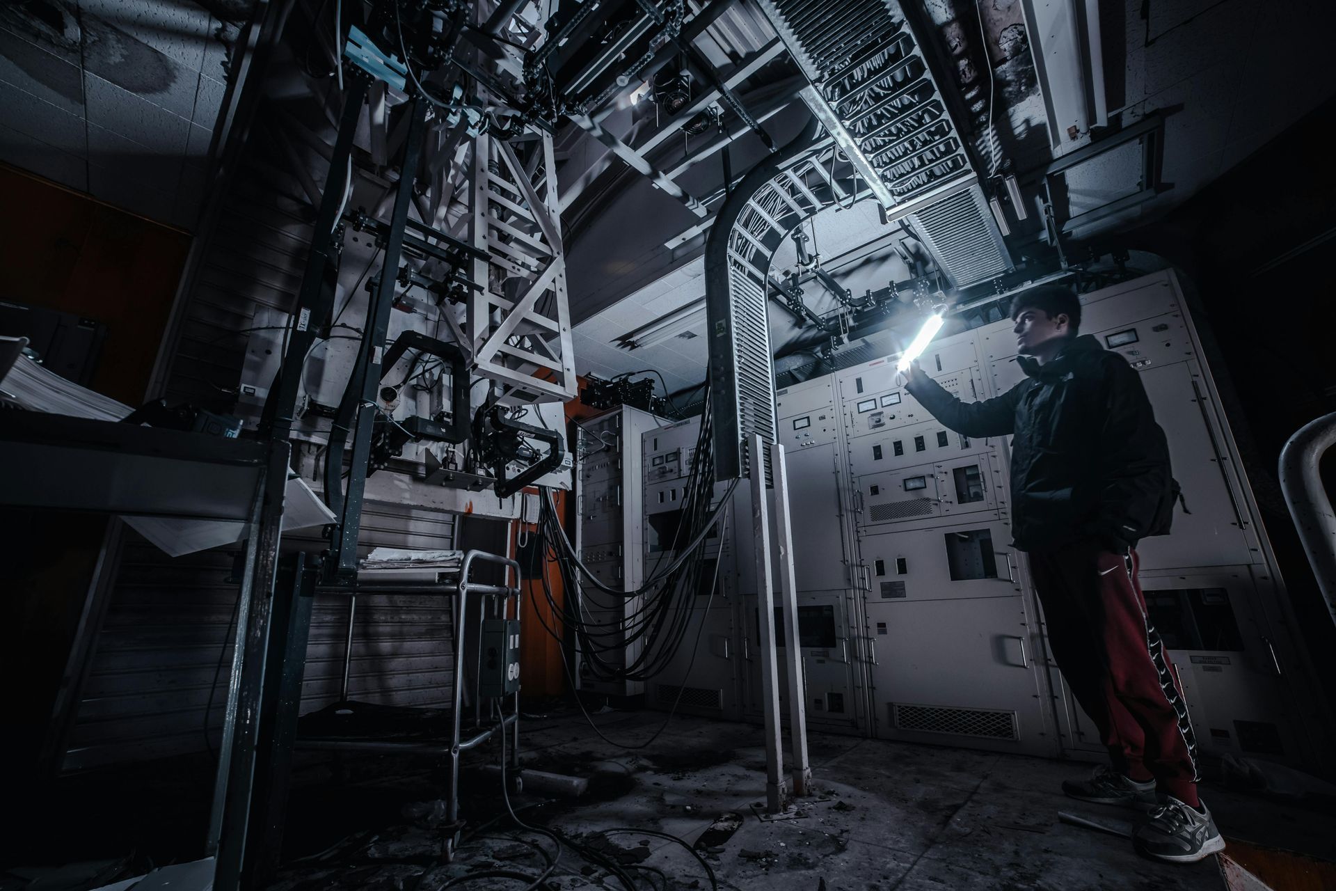 A person examines equipment in a dimly lit, industrial setting, holding a glowing light.