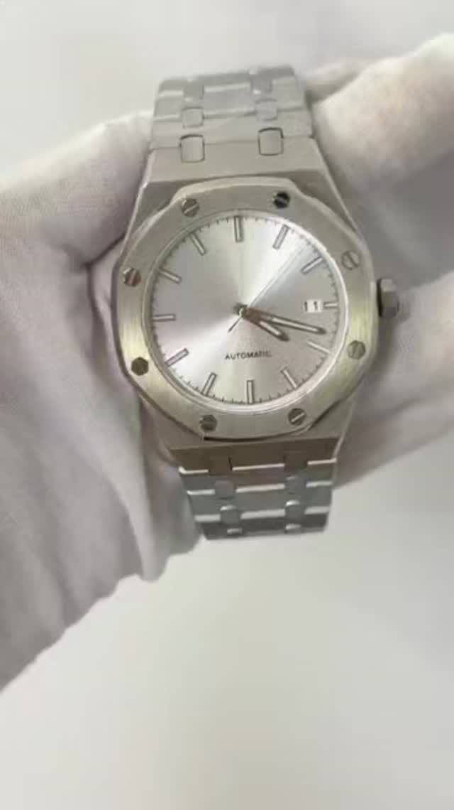 Reloj de pulsera plateado con brazalete de acero, sostenido por una mano enguantada.