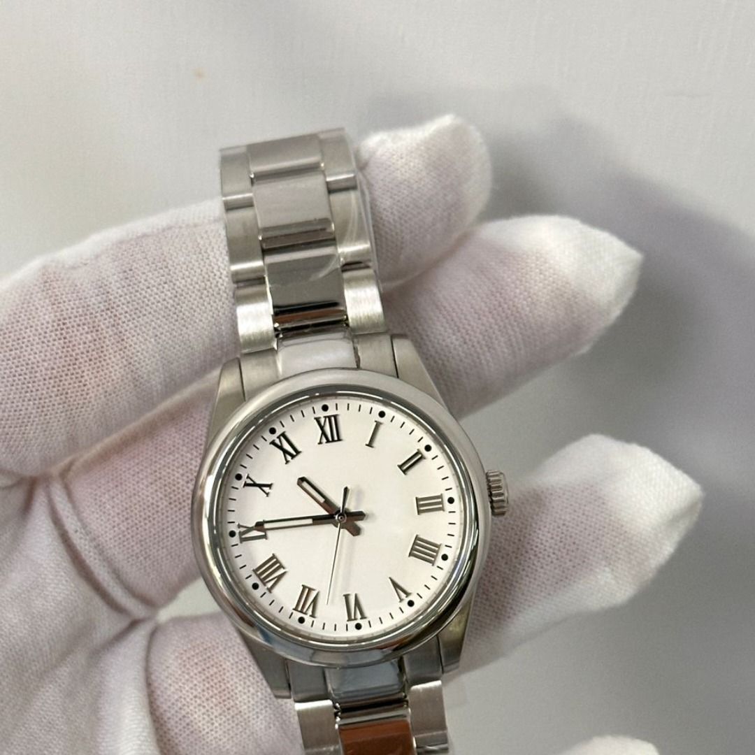 Reloj de pulsera plateado con esfera blanca, números romanos y correa de metal sujetado por una mano enguantada.