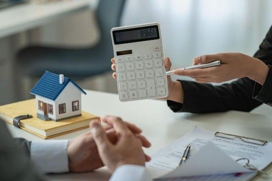 Person holding calculator during home loan consultation beside a small house model on a desk