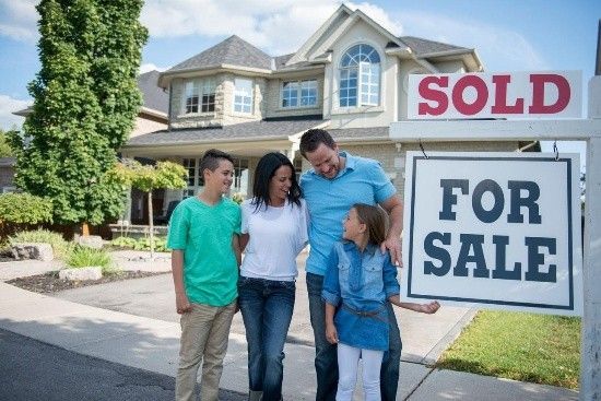 Family standing by a sold home sign in front of a suburban house