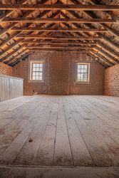 An empty attic with a wooden floor and brick walls.