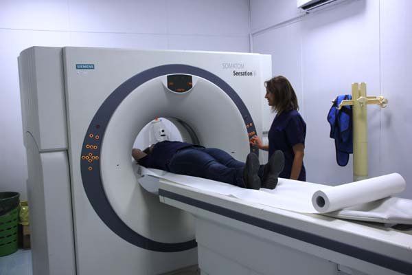 Una donna è in piedi accanto a un uomo disteso su una macchina per la TAC.