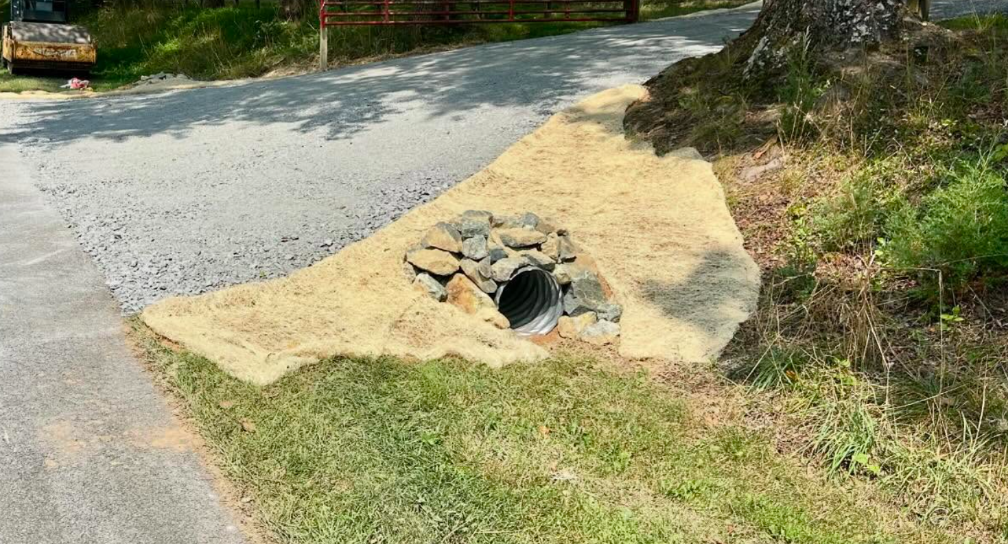 Night view of a yellow construction roller on a freshly laid road. Headlights illuminate the textured surface.