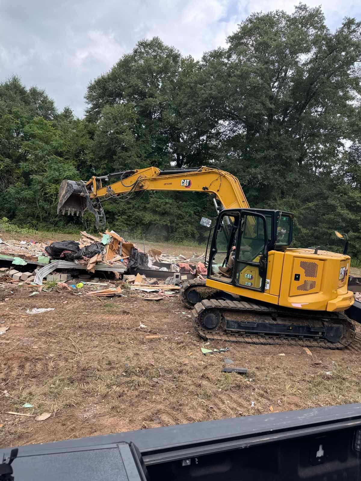 Excavator bucket removing a tree trunk in a wooded area.