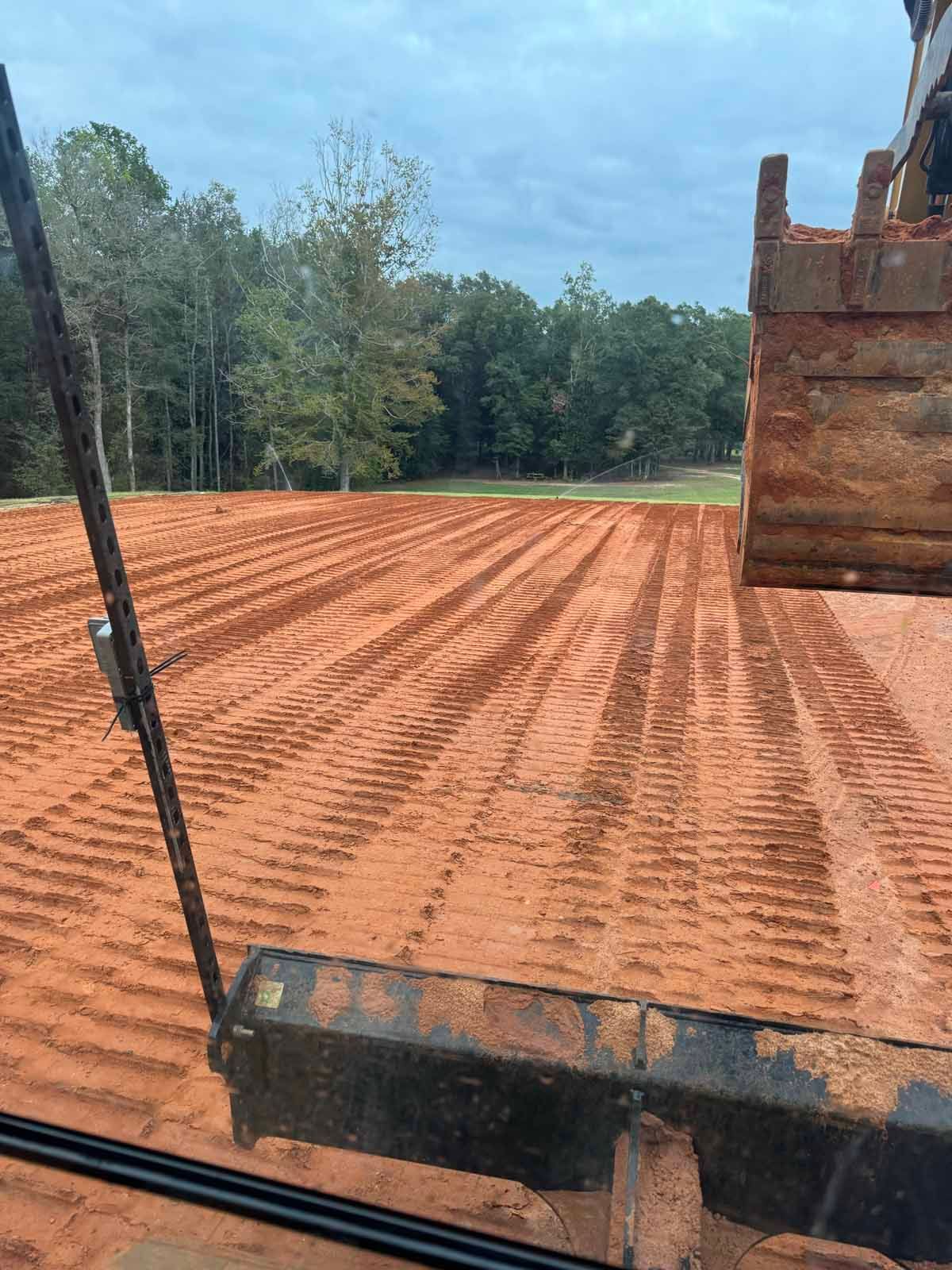 A John Deere tractor smoothing gravel on a winding driveway, surrounded by trees and a fence.
