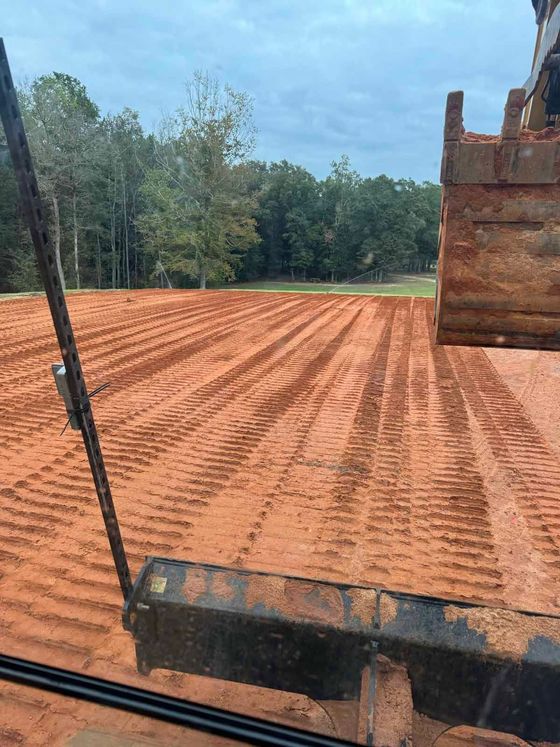 A John Deere tractor smoothing gravel on a winding driveway, surrounded by trees and a fence.