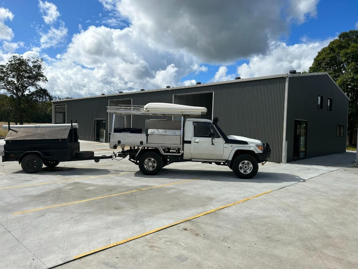 A White Truck With a Trailer Attached to It is Parked in Front of a Building — Mbah Metal Roofing in South Murwillumbah, NSW