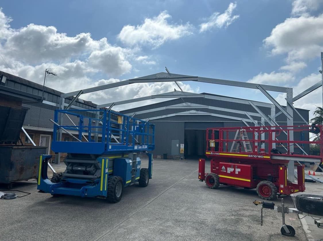 Two Scissor Lifts are Parked in Front of a Building — Mbah Metal Roofing in South Mullumbimby, NSW