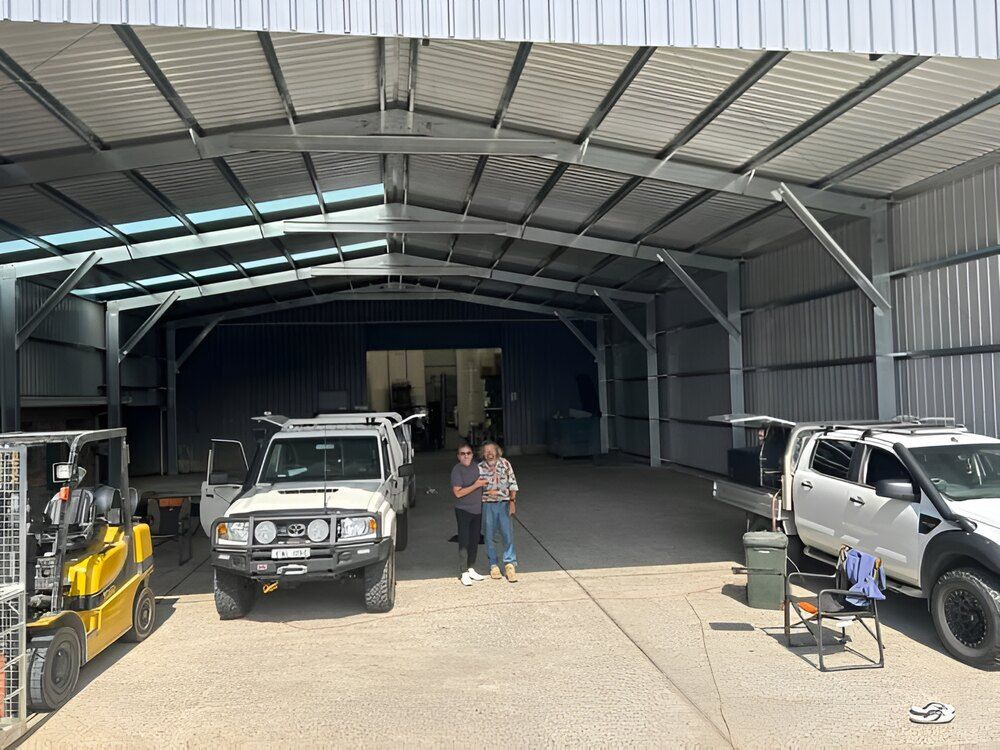 A Couple Of People Standing In Front Of A Warehouse With A Forklift — Mbah Metal Roofing In Murwillumbah, NSW