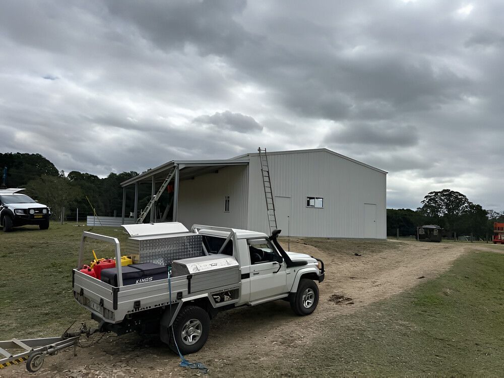 A White Truck With A Trailer Attached To It Is Parked In Front Of A Building — Mbah Metal Roofing In Murwillumbah, NSW