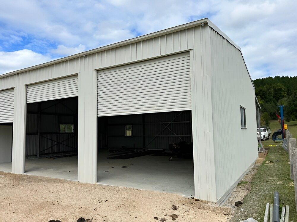 A Large White Building With Three Garage Doors Is Being Built — Mbah Metal Roofing In Murwillumbah, NSW