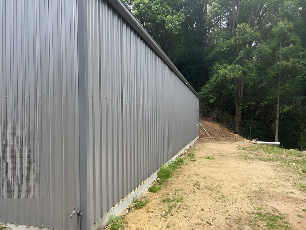 A Large Metal Building Is Sitting In The Middle Of A Dirt Field — Mbah Metal Roofing In Murwillumbah, NSW