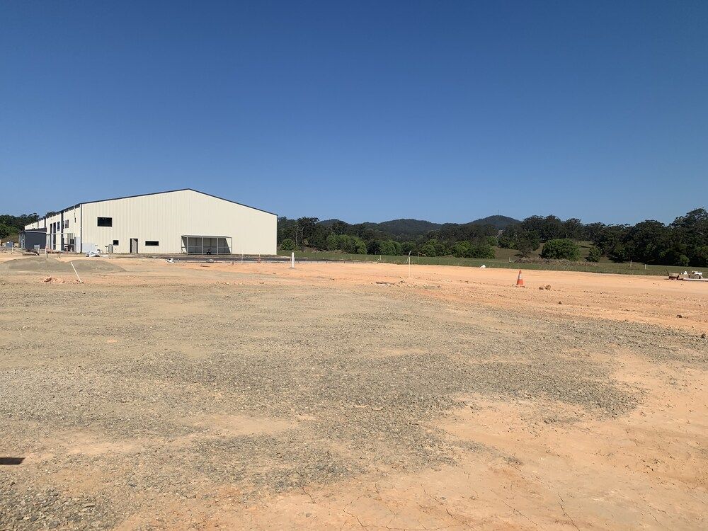 A Large White Building In The Middle Of A Dirt Field — Mbah Metal Roofing In Murwillumbah, NSW