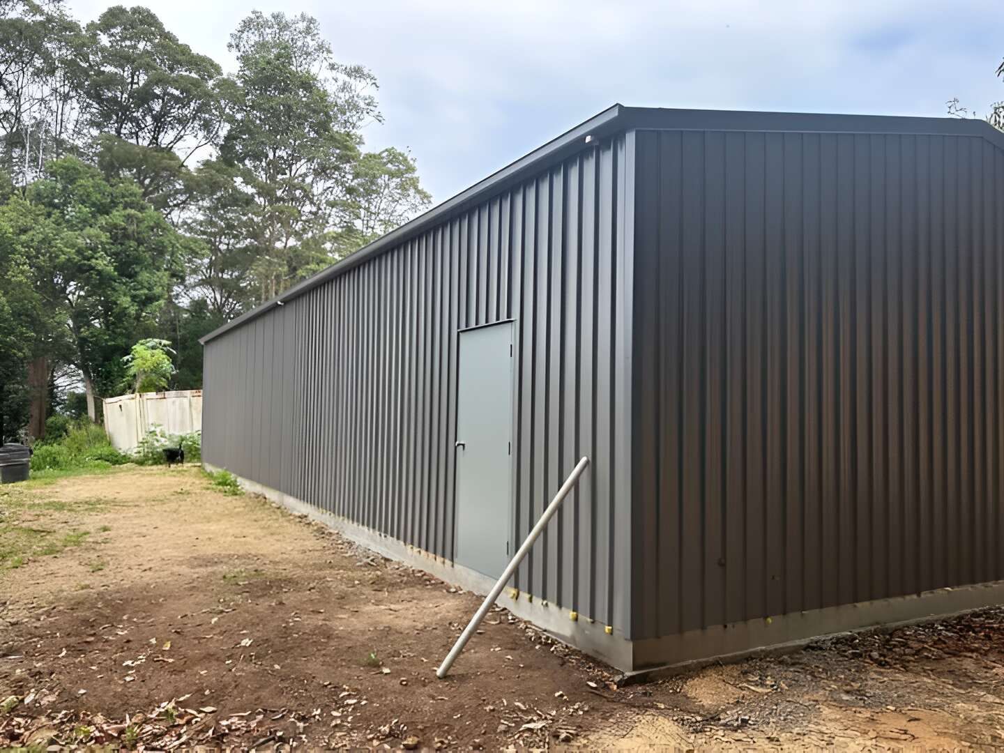A Large Metal Building With A Door In The Backyard — Mbah Metal Roofing In Murwillumbah, NSW