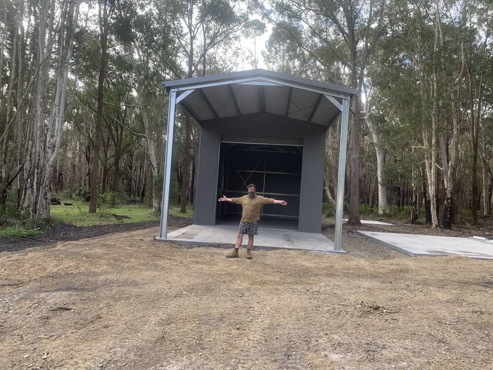 A Man Is Standing In Front Of A Garage In The Woods— Mbah Metal Roofing In Murwillumbah, NSW