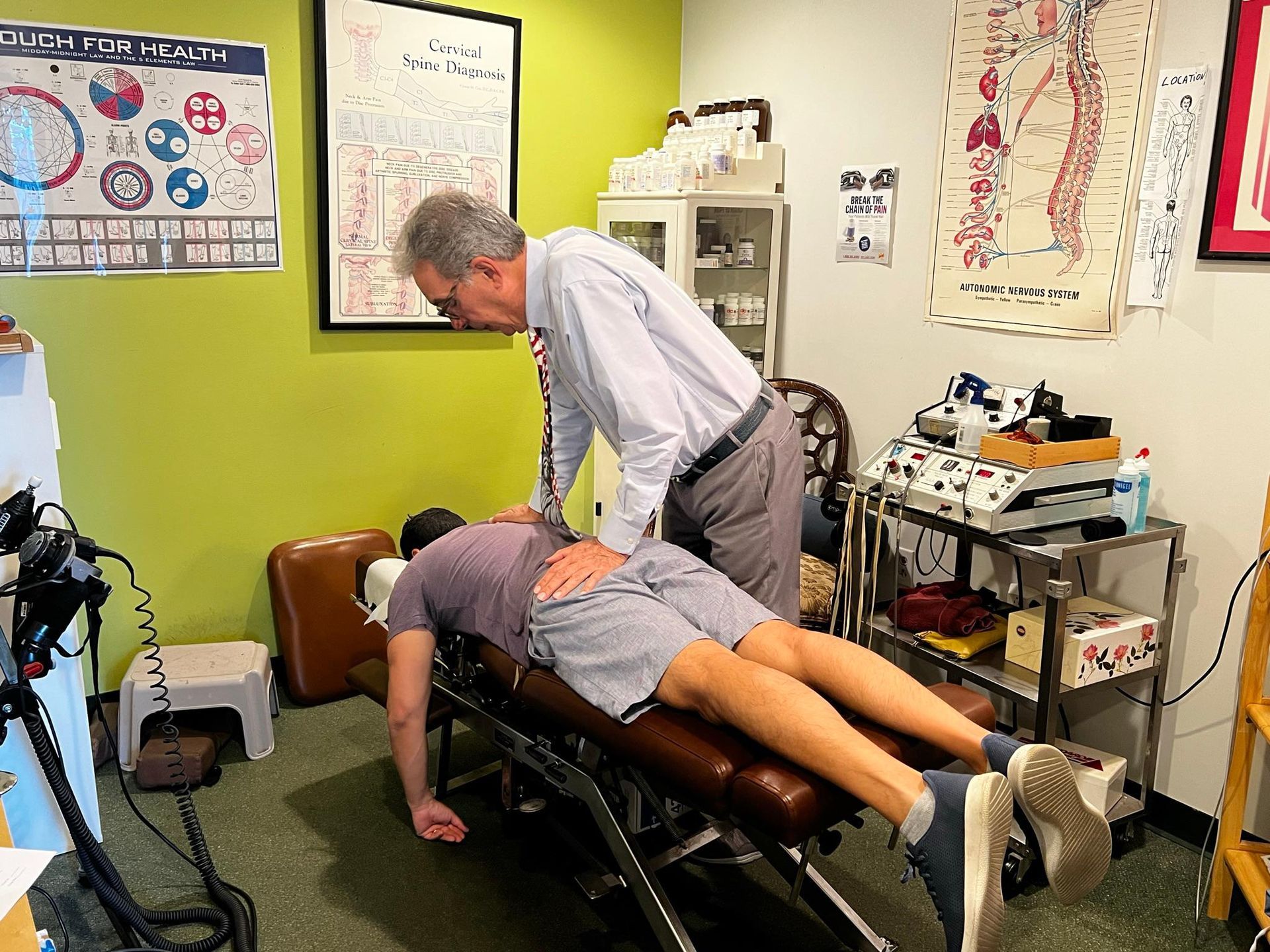 A chiropractor in a button-down shirt performs an adjustment on a person lying face down on a treatment table.