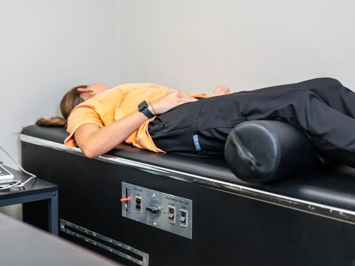 A person lying on a mechanical treatment table with a bolster under their knees in a clinical setting.
