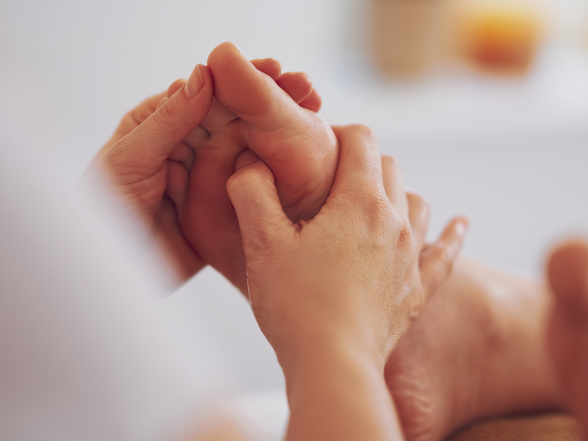 A person performing a therapeutic foot massage, with hands applying pressure to the sole of the foot.