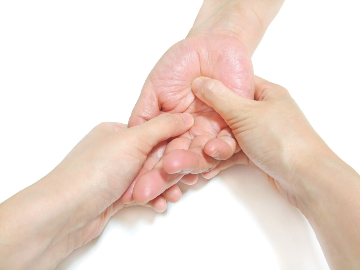 Two hands provide a gentle massage to the palm of another hand against a plain white background.