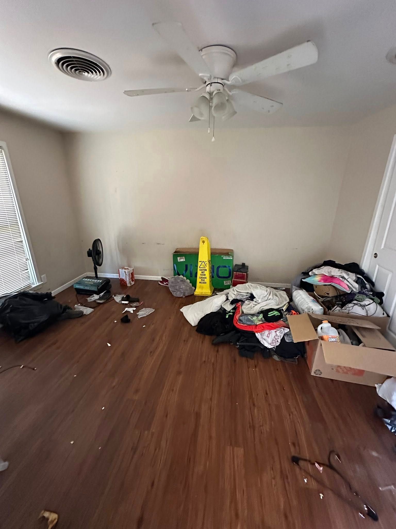 Room with cluttered floor, ceiling fan, and window with blinds.