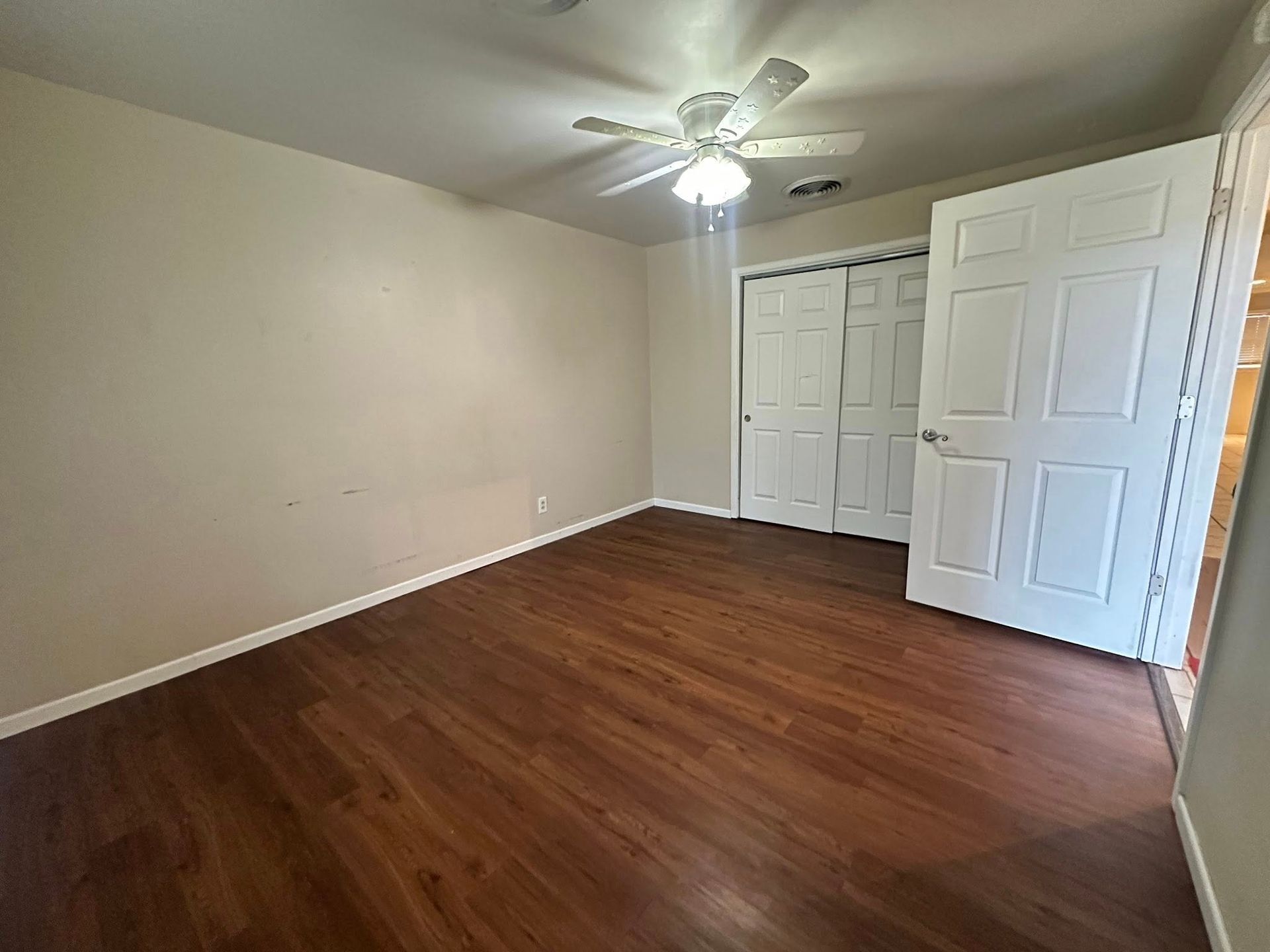 Empty room with brown flooring, light walls, a ceiling fan, and white closet/door.