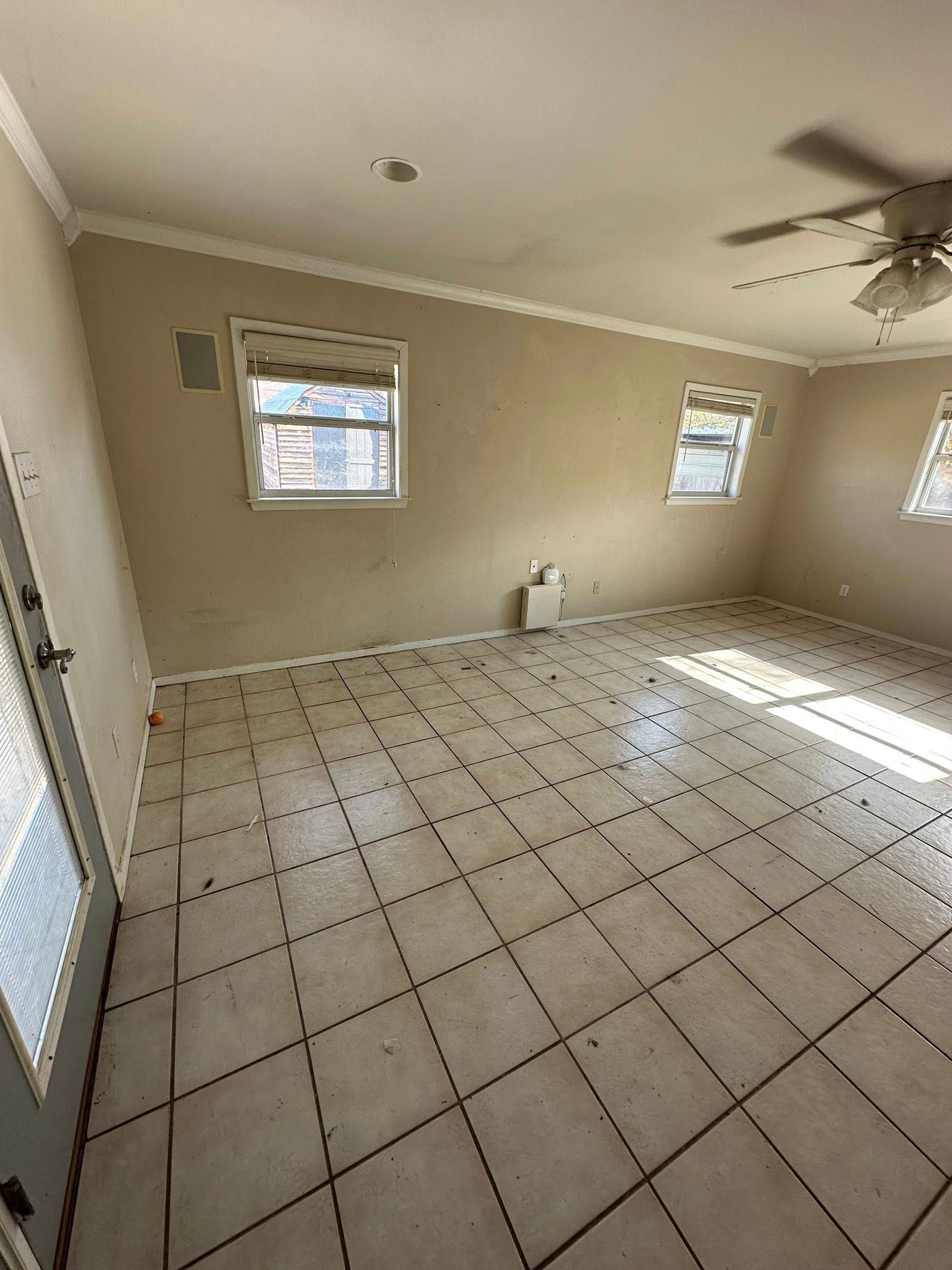 Empty room with beige walls, tile floor, and three windows.