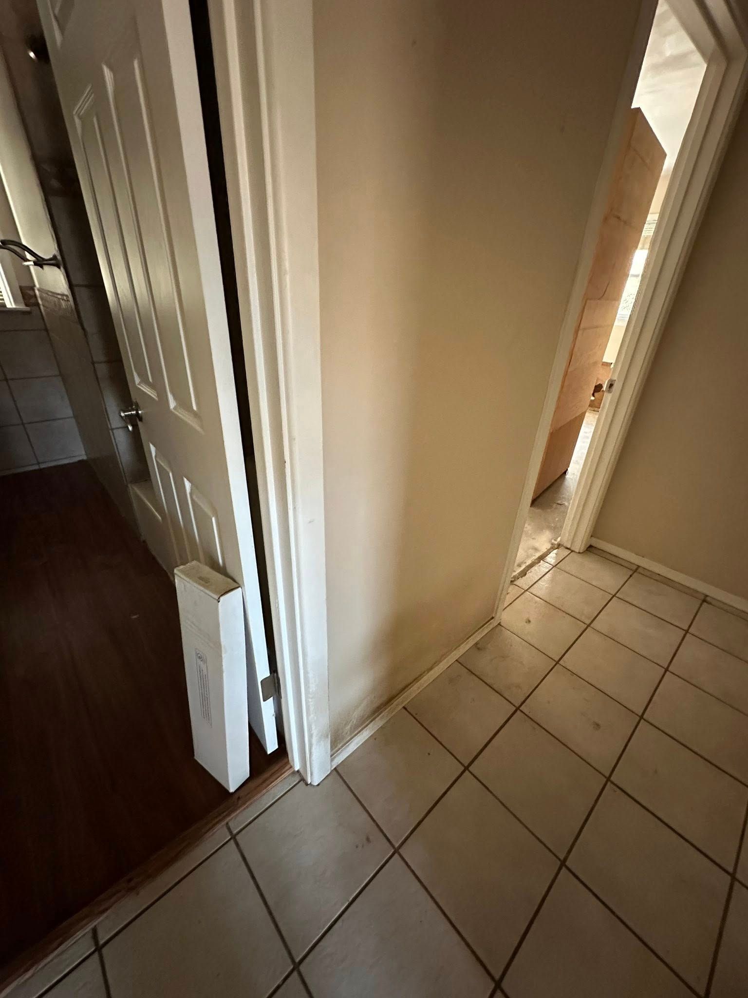 Open doorway into a hallway with a tiled floor, another door is visible, and a partially open door with a white trim is on the left.