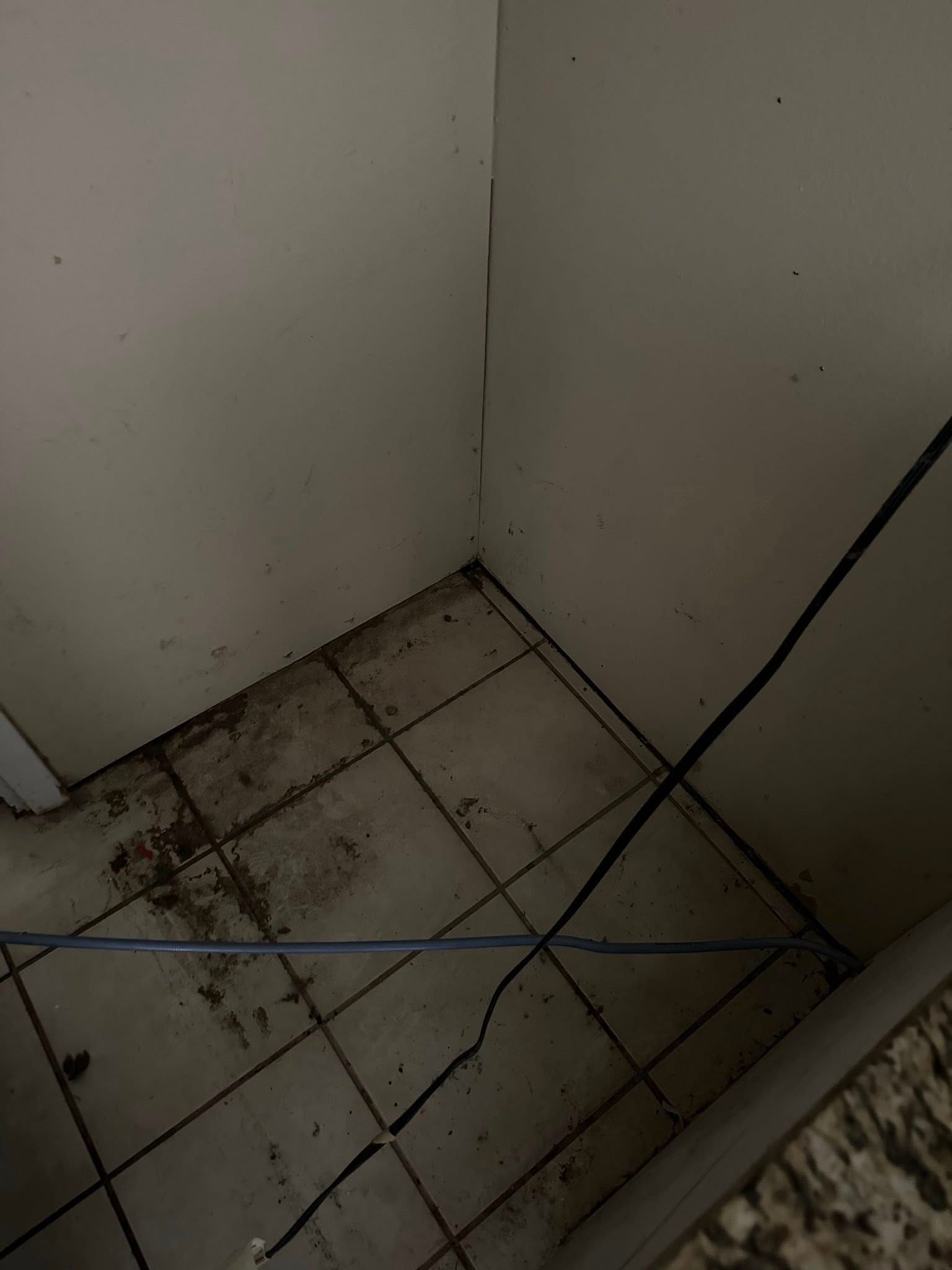 Dirty corner with tiled floor and wires. Brown stains and dirt. Dark walls.